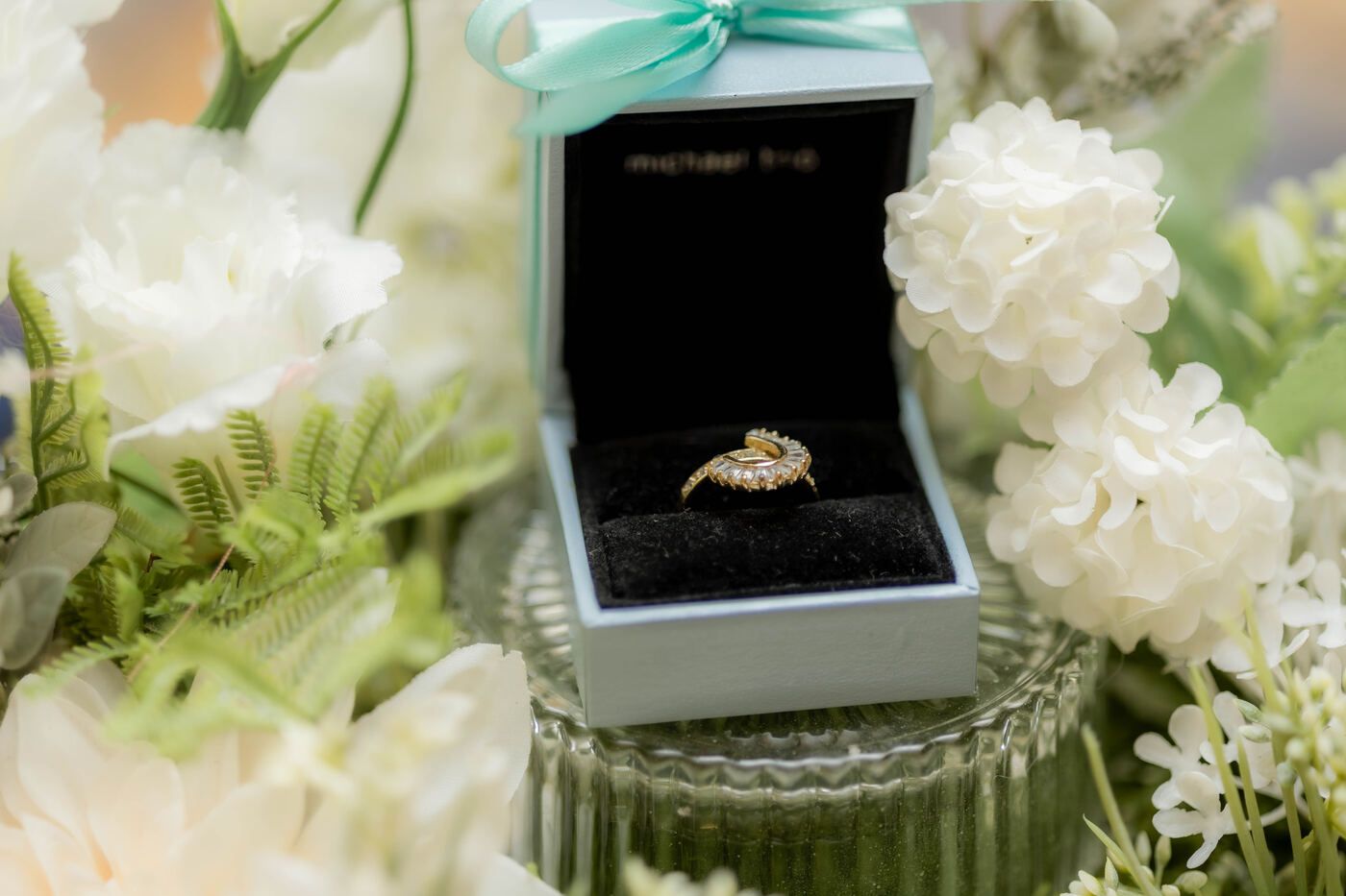 Wedding ring displayed in a black ring box among white florals