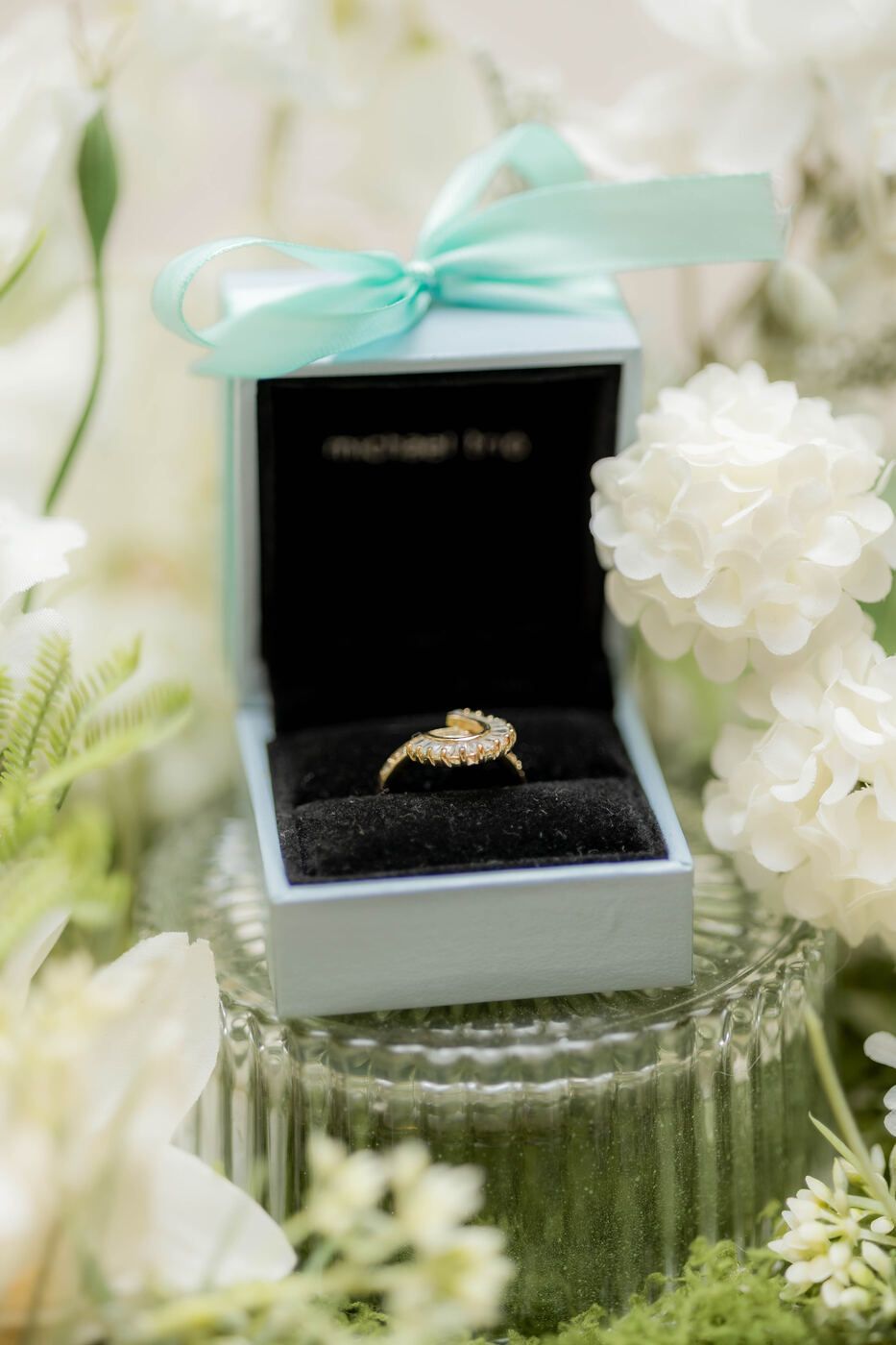 Wedding ring display in a black box with white florals